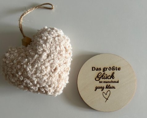 Ein weiches, beiges Herz und ein Holzstück mit dem Text: „Das größte Glück, das es gibt.“