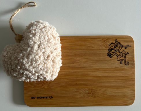 Holzbrett mit einem Herzen aus heller Wolle und einem grafischen Design.