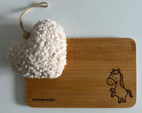 Holzbrett mit eingraviertem Pferd und einem grauen, herzförmigen Kissen.