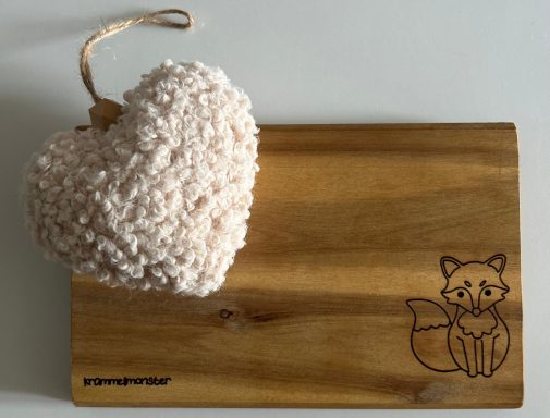 Herz aus Wolle auf einer Holzplatte mit einem eingelegten Fuchs-Motiv.