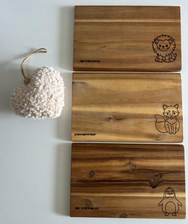 Drei Holzschneidebretter mit Tiermotiven und ein herzförmiger, rosa Dekoartikel.