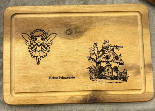 Holzbrett mit einem Feen-Motiv und einem kleinen Pilzhaus.