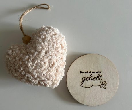 Ein beigefarbenes Herz aus Wolle neben einem runden Holzstück mit der Aufschrift "gönn dir".
