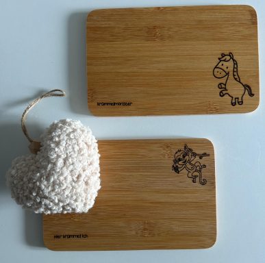 Zwei Holzuntersetzer mit Tiermotiven und ein weißes, herzförmiges Dekorationselement.