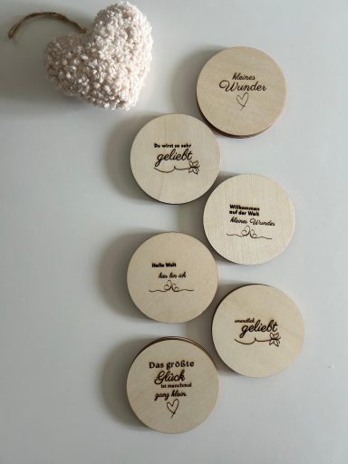 Sechs runde Holzscheiben mit verschiedenen Schriftzügen und ein Herz aus kleinen, weißen Perlen.