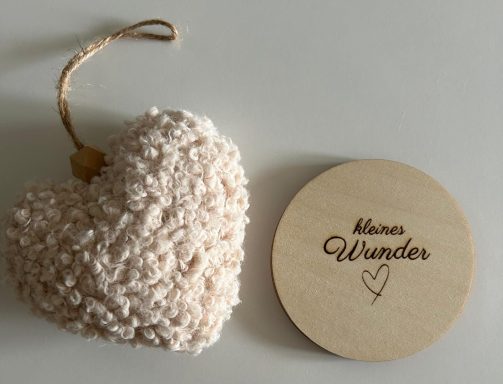 Ein weiches, beige Herz und ein runder Holzanhänger mit der Aufschrift "Wunder".